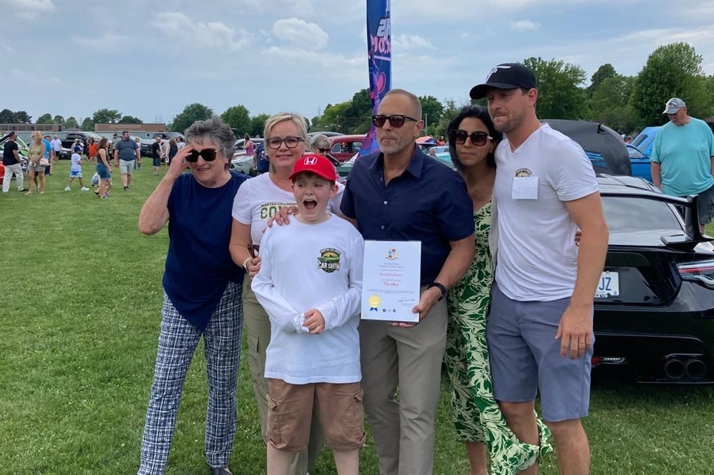 Group poses for photo at outdoor car show on grass